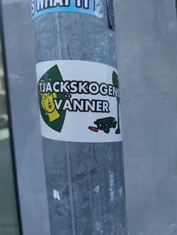 A sticker featuring a logo with a woman's face, text that says "Tjackskogens Vänner", and a picnic table with a red object next to it. The text appears to be Swedish.