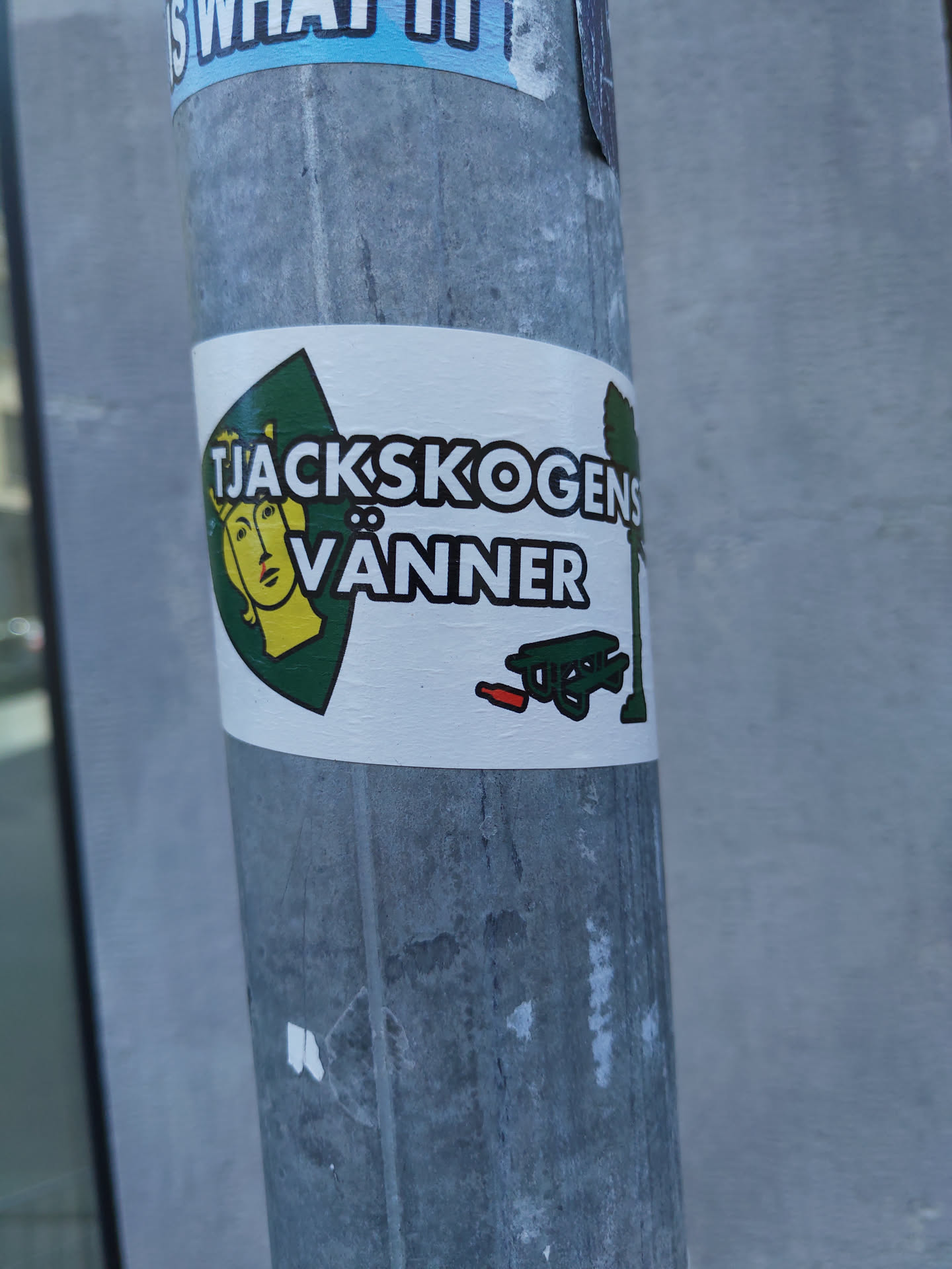 A sticker featuring a logo with a woman's face, text that says "Tjackskogens Vänner", and a picnic table with a red object next to it. The text appears to be Swedish.