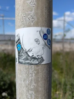 This sticker shows a black and white sketch of a person licking a boot. The boot has a blue flower on it. To the right of the head is a vertical stack of blue circles, each containing a letter: K, D, M, and L.