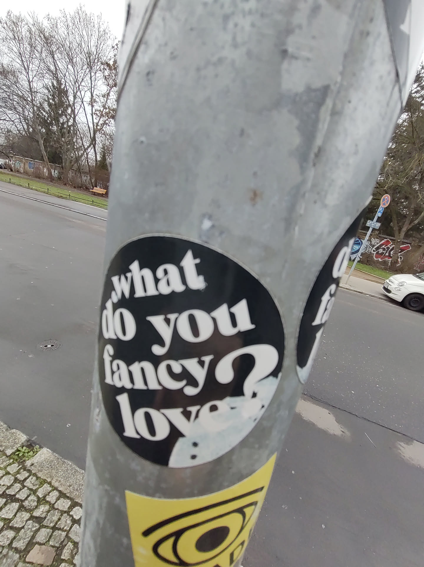 A round black and white sticker on a metal pole. The text on the sticker is in a retro style font.