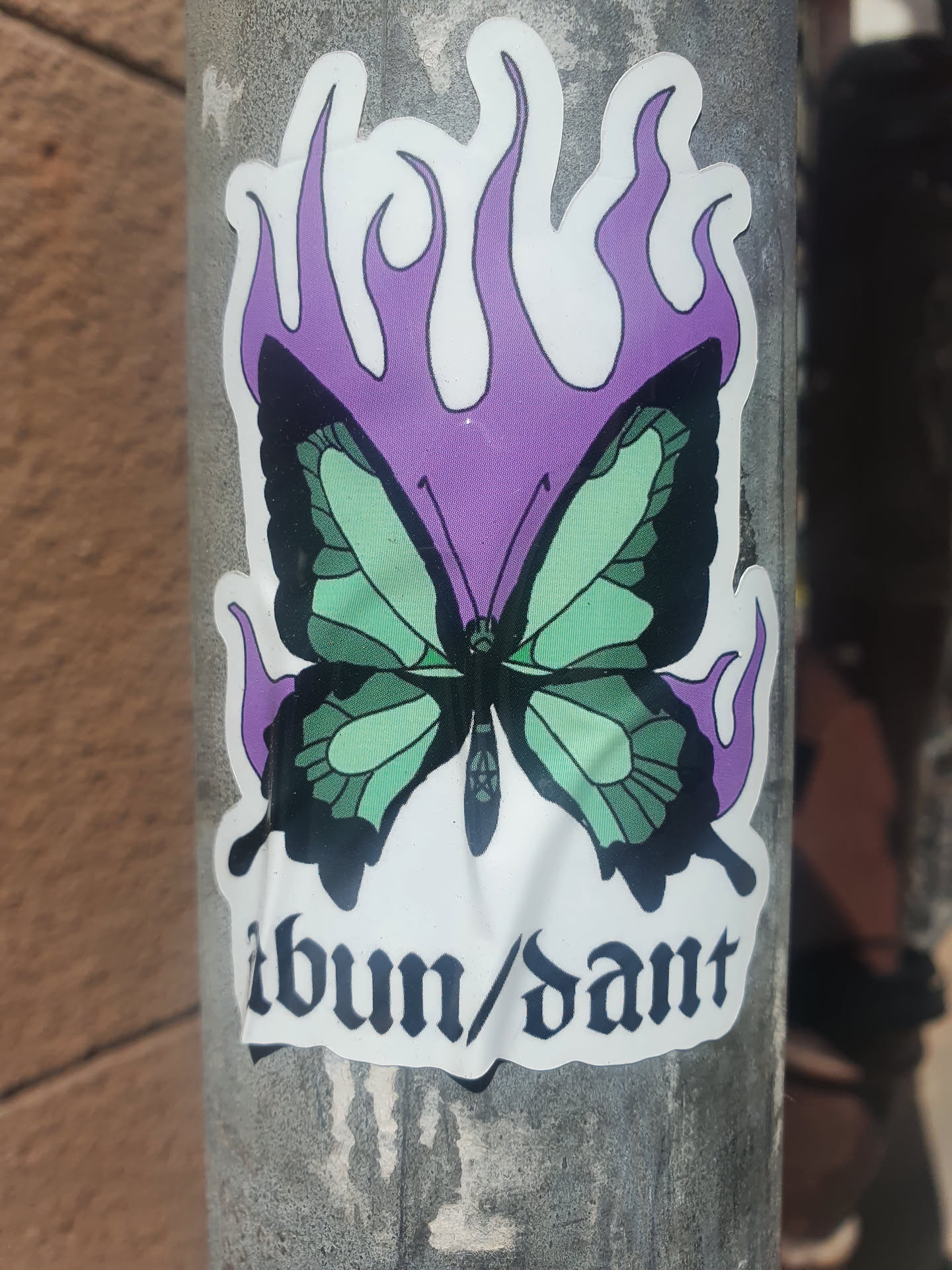 A sticker featuring a butterfly engulfed in purple flames. The word Abundant is written in a gothic-style font at the bottom. 