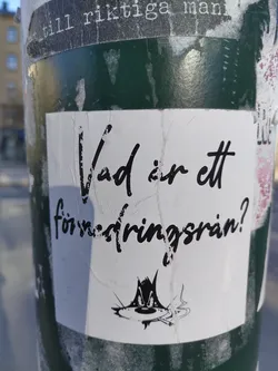 A sticker with a question in Swedish: "Vad är ett försäkringsbrån?" (What is an insurance fraud?). It features a cartoon drawing of a cat smoking a cigarette.