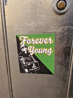 A sticker featuring a stylized illustration of a person carrying a box, with the text 'Forever Young' in a vintage-style font. The sticker has a green and black color scheme.  The box appears to have a brewery logo on it, possibly Elm Brew.