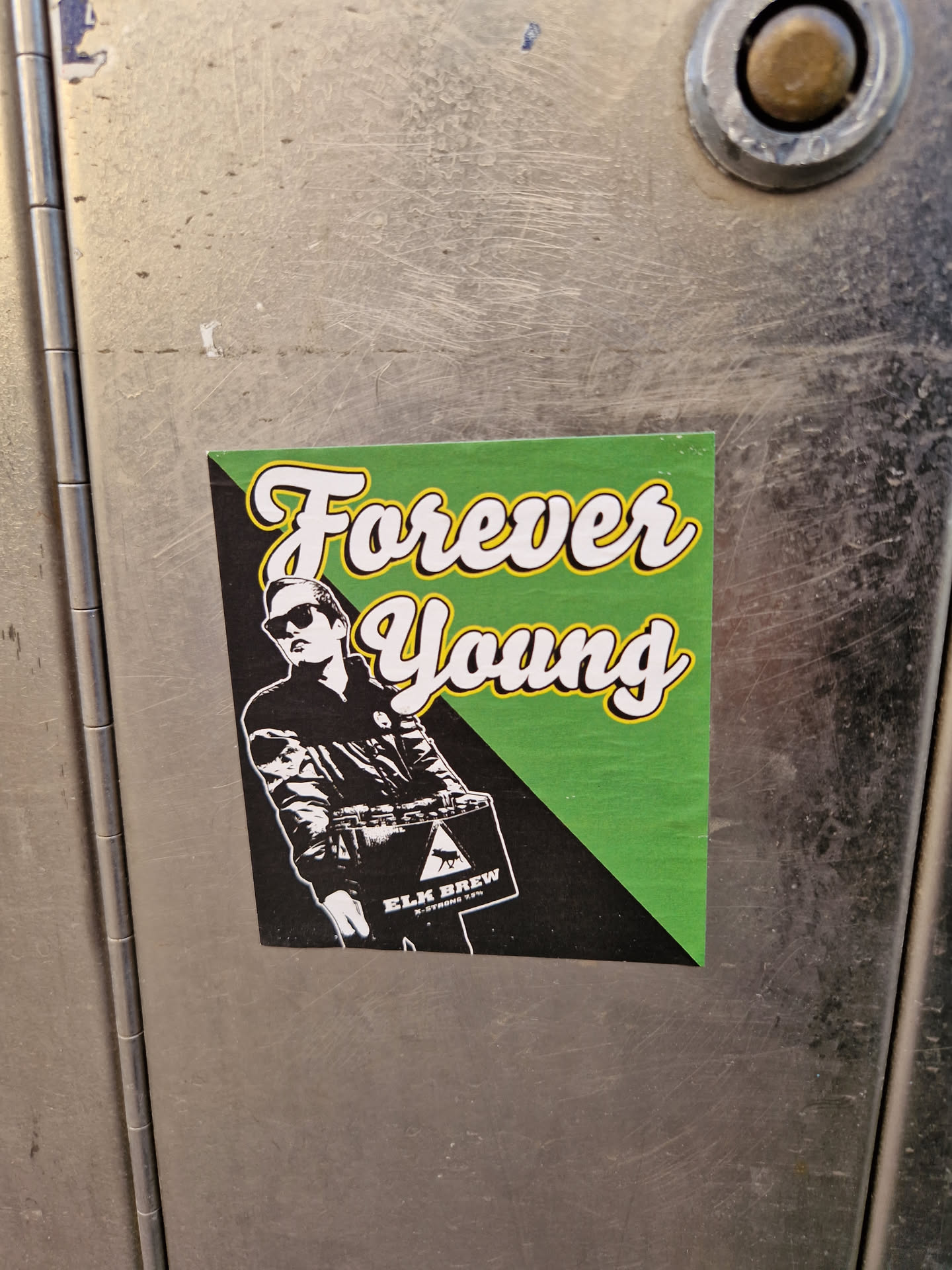 A sticker featuring a stylized illustration of a person carrying a box, with the text 'Forever Young' in a vintage-style font. The sticker has a green and black color scheme.  The box appears to have a brewery logo on it, possibly Elm Brew.