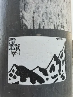 Black and white sticker with a mountain range illustration and text. The text on the left says "Long Live Mermaid Killer" and the year 2021 is written on the top right corner. The sticker features a simple design with a stylized mountain landscape.
