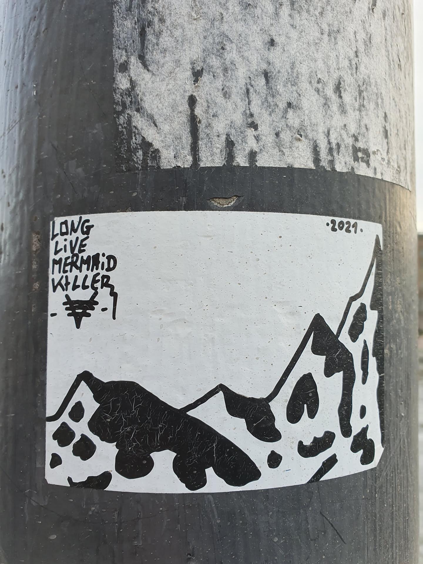 Black and white sticker with a mountain range illustration and text. The text on the left says "Long Live Mermaid Killer" and the year 2021 is written on the top right corner. The sticker features a simple design with a stylized mountain landscape.