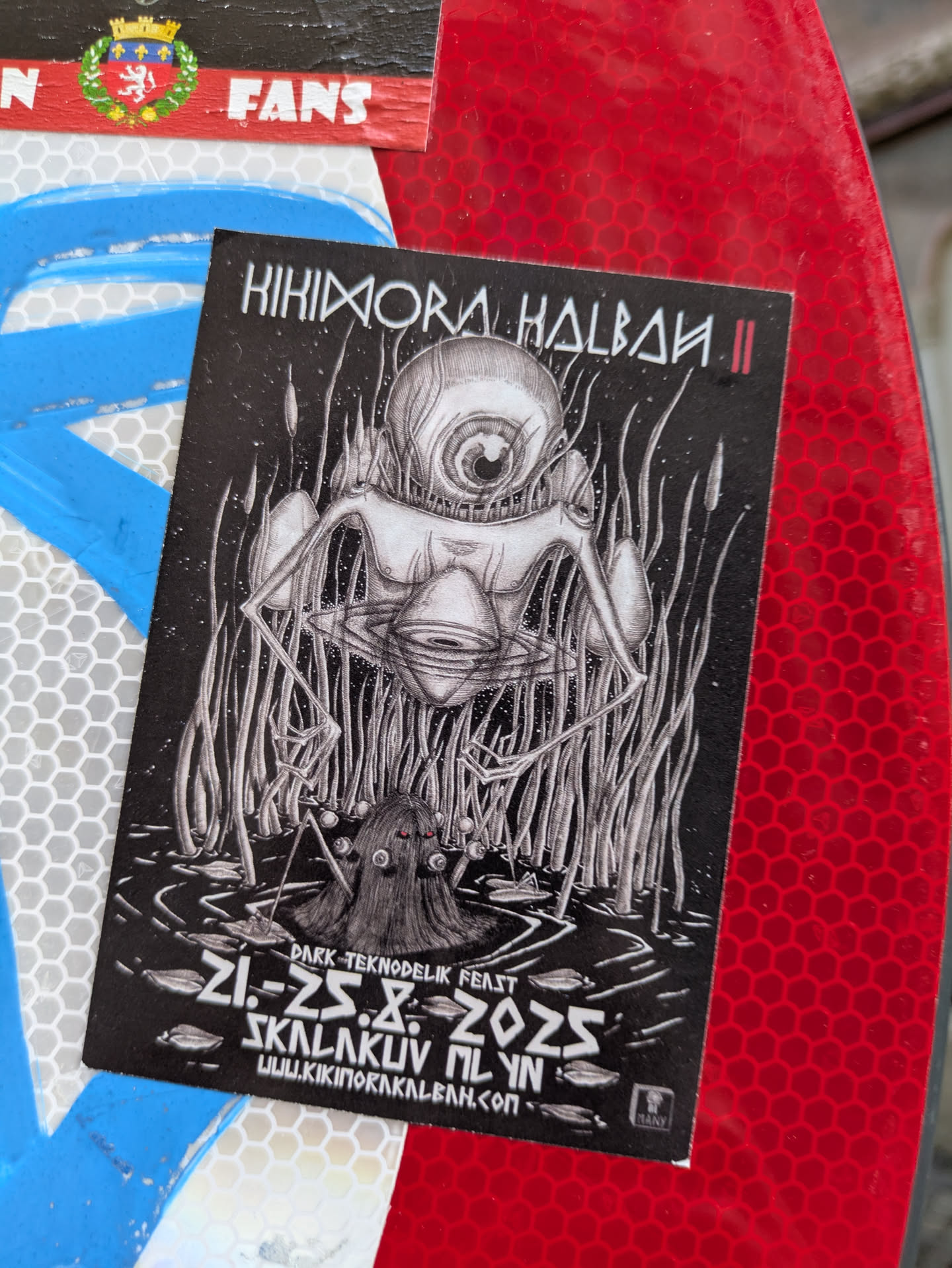 The sticker features a black and white illustration of surreal creatures in a swampy landscape, with the event details provided at the bottom.