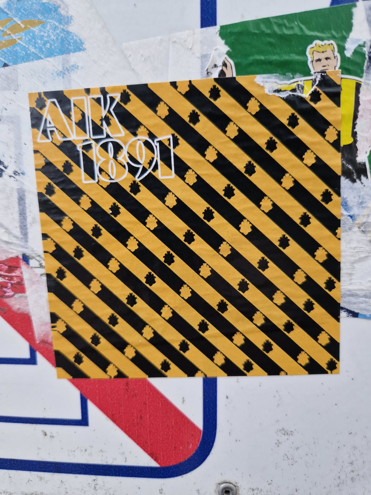 This sticker features the letters AIK and the number 1891 in a bold, sans-serif font.  The background is a repeating pattern of diagonal black and yellow stripes, with small, stylized black shapes scattered throughout.  The color scheme is reminiscent of caution tape or warning signs.