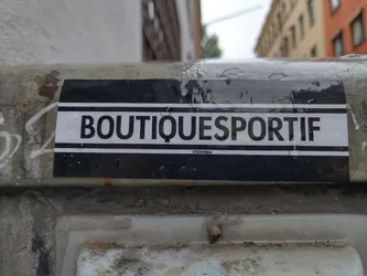 A black and white sticker with the text "BOUTIQUESPORTIF" and "STOCKHOLM" in smaller text underneath. The sticker is attached to a weathered surface.