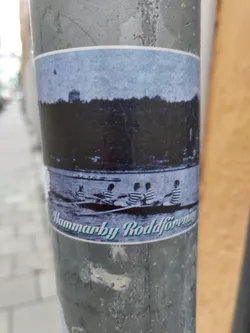 A sticker featuring a historical black and white image of several people rowing a boat on a lake or river. The text at the bottom reads "Hammarby Roddförening".