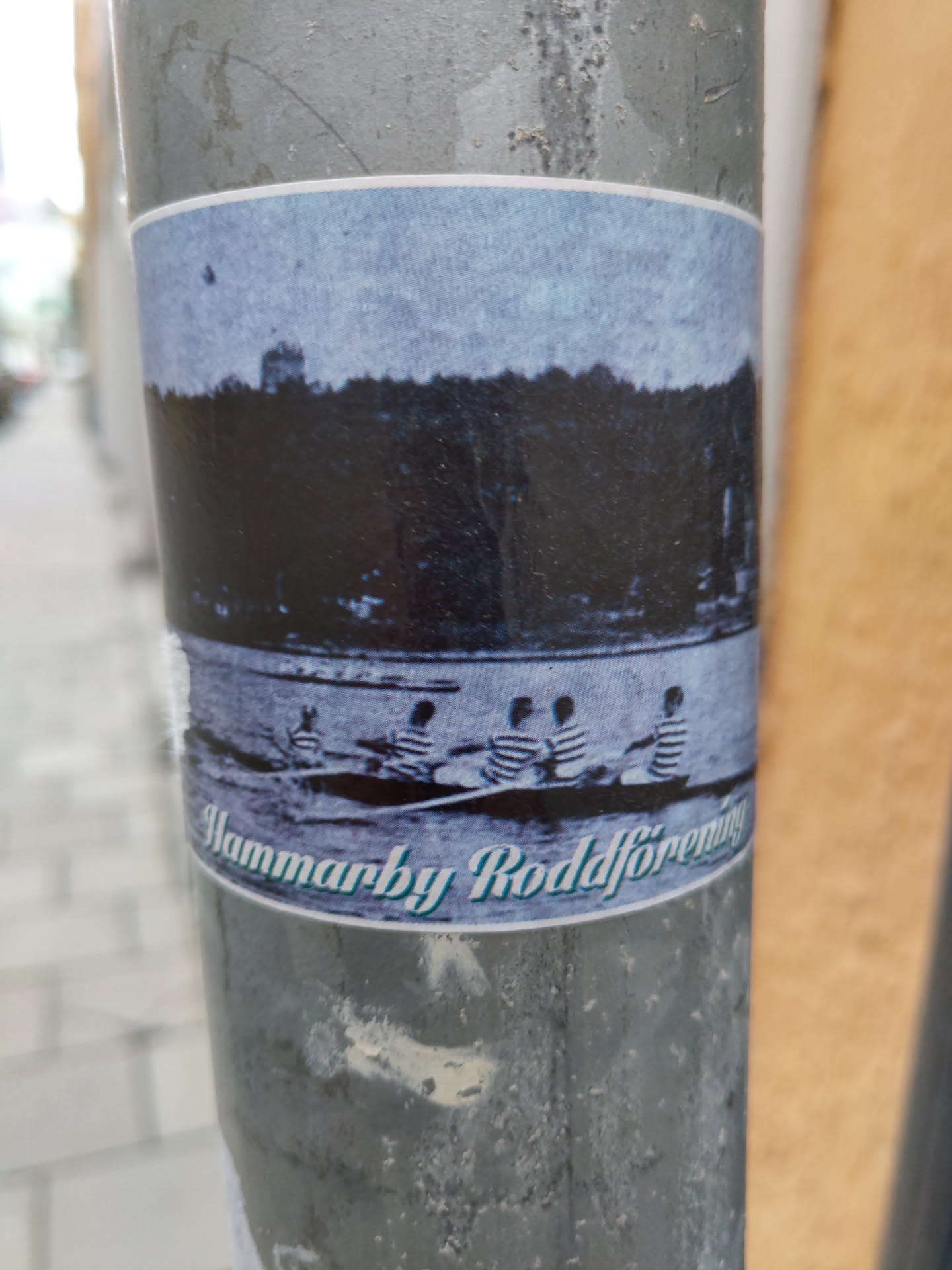 A sticker featuring a historical black and white image of several people rowing a boat on a lake or river. The text at the bottom reads "Hammarby Roddförening".