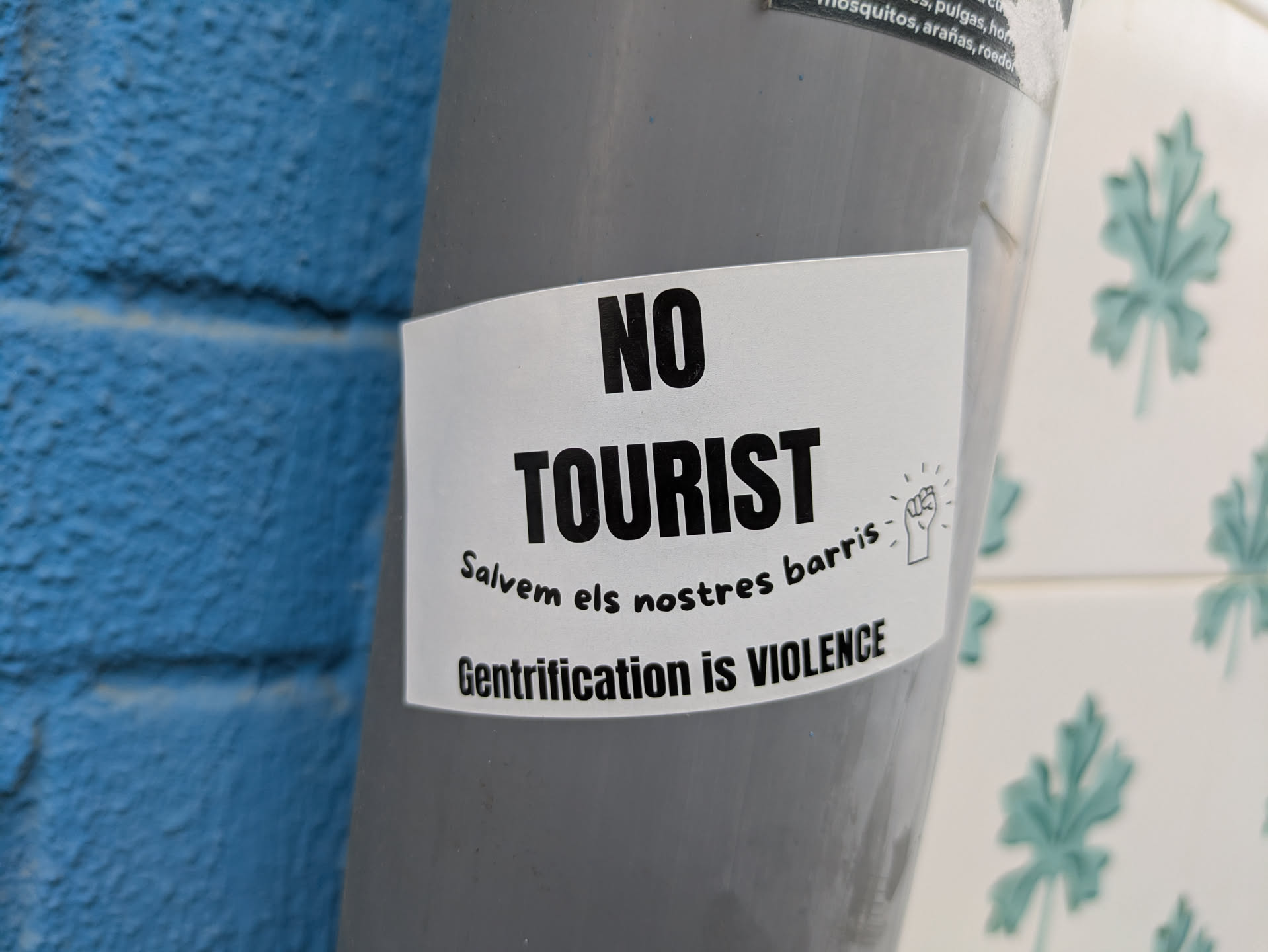 The sticker features the text 'NO TOURIST' in bold, followed by 'Salvem els nostres barris' and 'Gentrification is VIOLENCE'. It includes a small illustration of a raised fist.