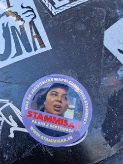 A round sticker featuring a photo of Jacqueline Mapel Cummings, with text that reads 'Stammisar' in large letters, and underneath, smaller text states 'På Bio 2 September' and the website www.stammisar.se. The sticker has a purple background and white text, and it's affixed to a dark surface with other stickers around it.