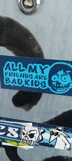This sticker has a blue background. It reads 'ALL MY FRIENDS ARE BAD KIDS' in a playful font. Next to the text, there's a cartoonish drawing of a head with wide eyes and a large, toothy grin, giving it a slightly sinister appearance.