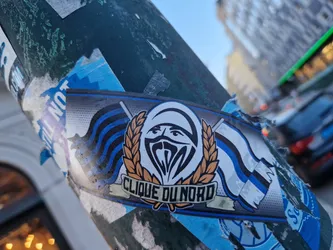 A sticker featuring the logo of Clique du Nord. The logo is a stylized face with a balaclava, surrounded by a wheat wreath and two stylized flags. The words "Clique du Nord" are written under the logo.