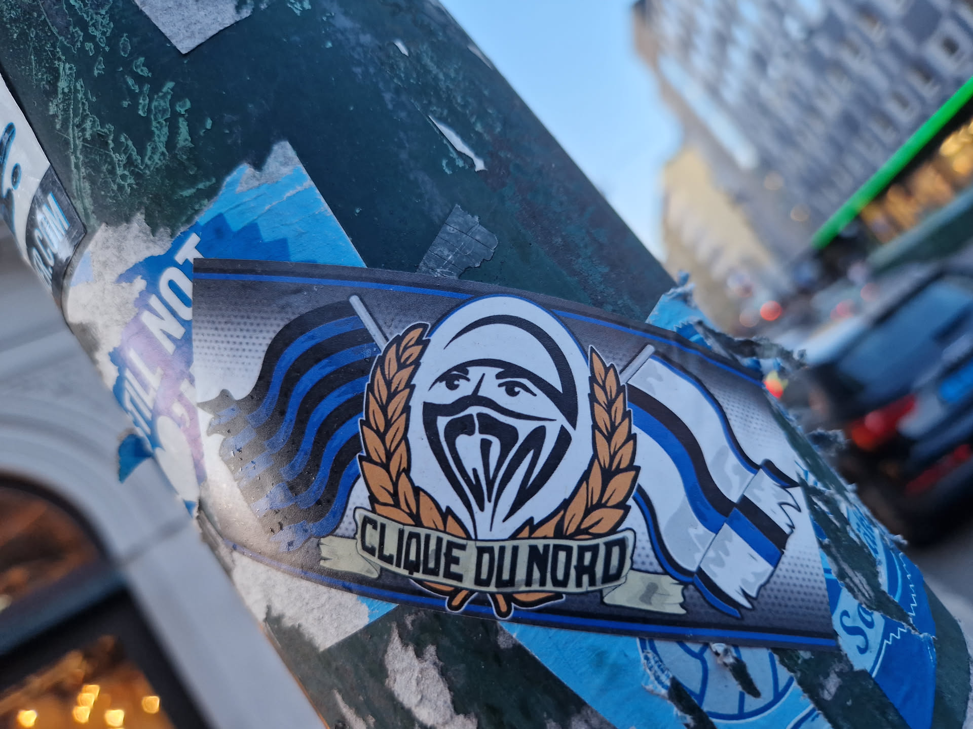 A sticker featuring the logo of Clique du Nord. The logo is a stylized face with a balaclava, surrounded by a wheat wreath and two stylized flags. The words "Clique du Nord" are written under the logo.