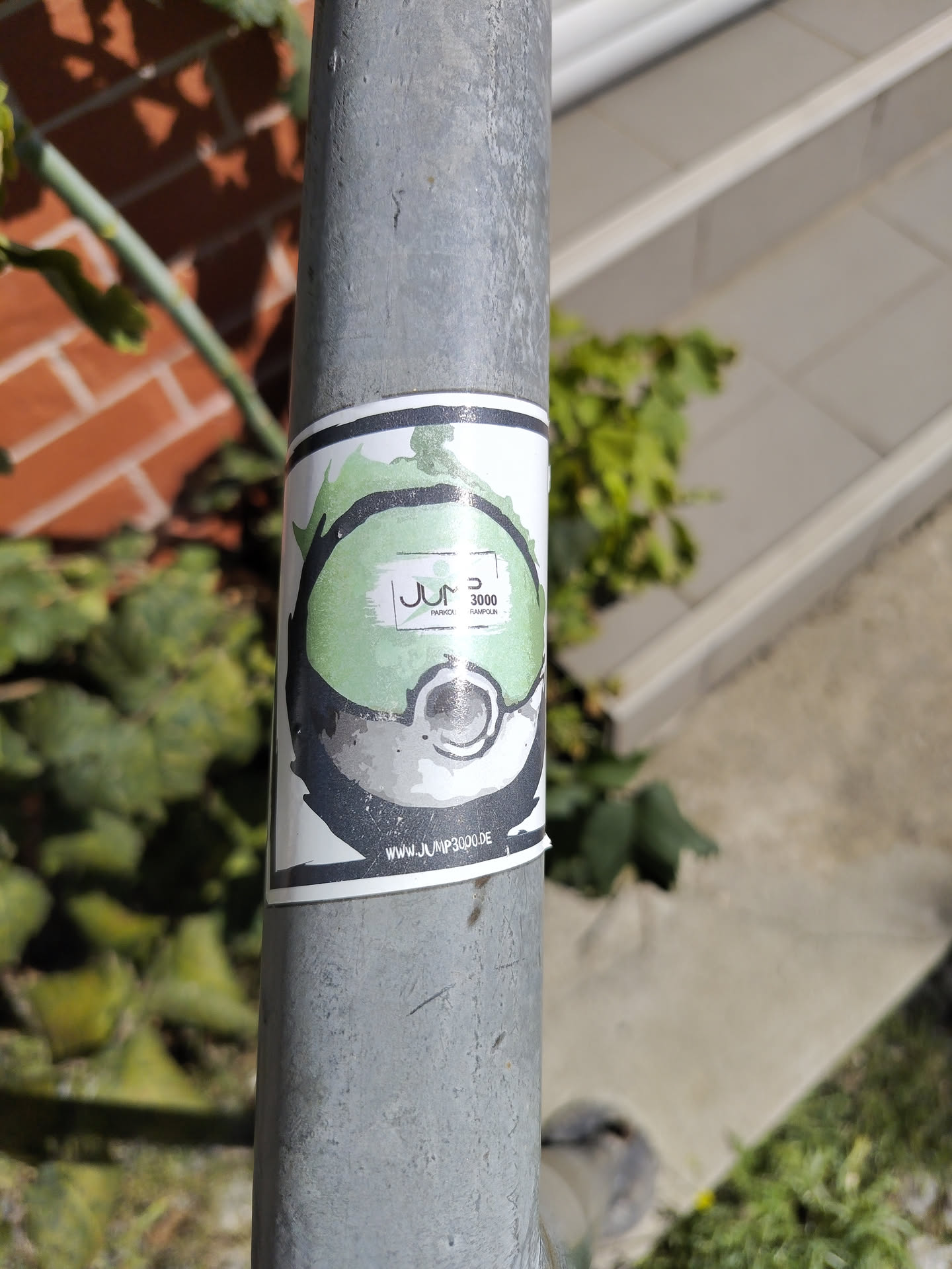 The sticker is circular with a white border. The main design features a stylized, abstract representation of a green and grey orb, possibly a Poké Ball or a similar game element, with a black outline. Inside the orb, there is a white rectangle containing the text 'JUMP 3000' in black. Below this, in smaller text, are the words 'PARKOUR' and 'TRAMPOLIN'. The bottom edge of the sticker displays a website address: 'WWW.JUMP3000.DE'. The overall aesthetic is modern and energetic.