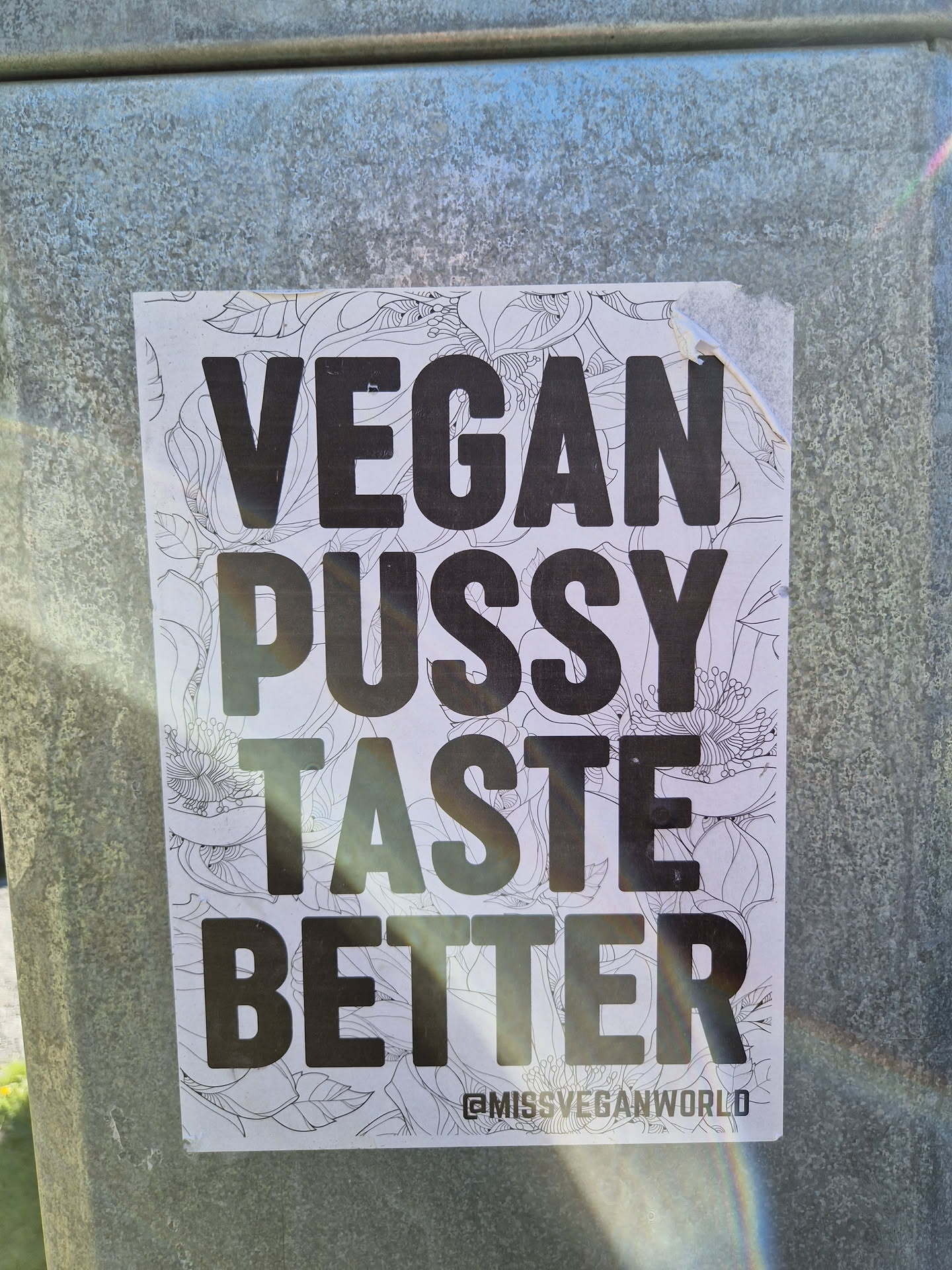 A sticker with a bold text message on a floral background. The text reads 'Vegan Pussy Taste Better' and includes a social media handle at the bottom.