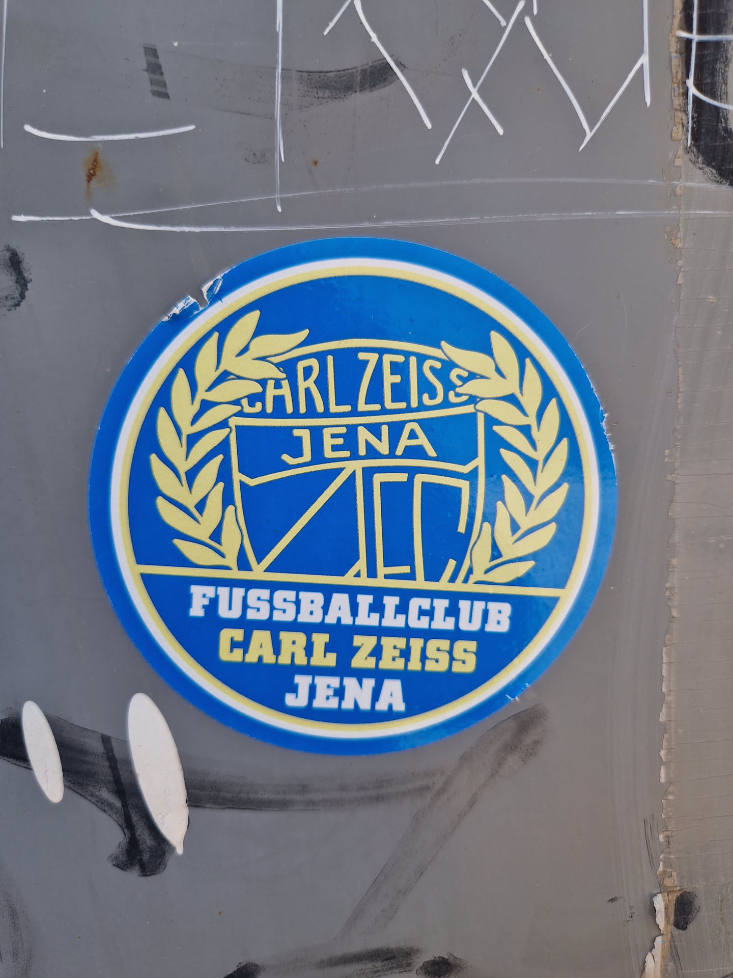 A round sticker featuring the logo of FC Carl Zeiss Jena, a German football club. The logo is predominantly blue and yellow, with text that says  'Carl Zeiss Jena' and 'Fussballclub Carl Zeiss Jena'.