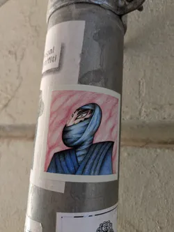 A sticker features a character wrapped in blue clothing against a pink background. The character's eyes are visible through an opening in the clothing, and their face is partially concealed.