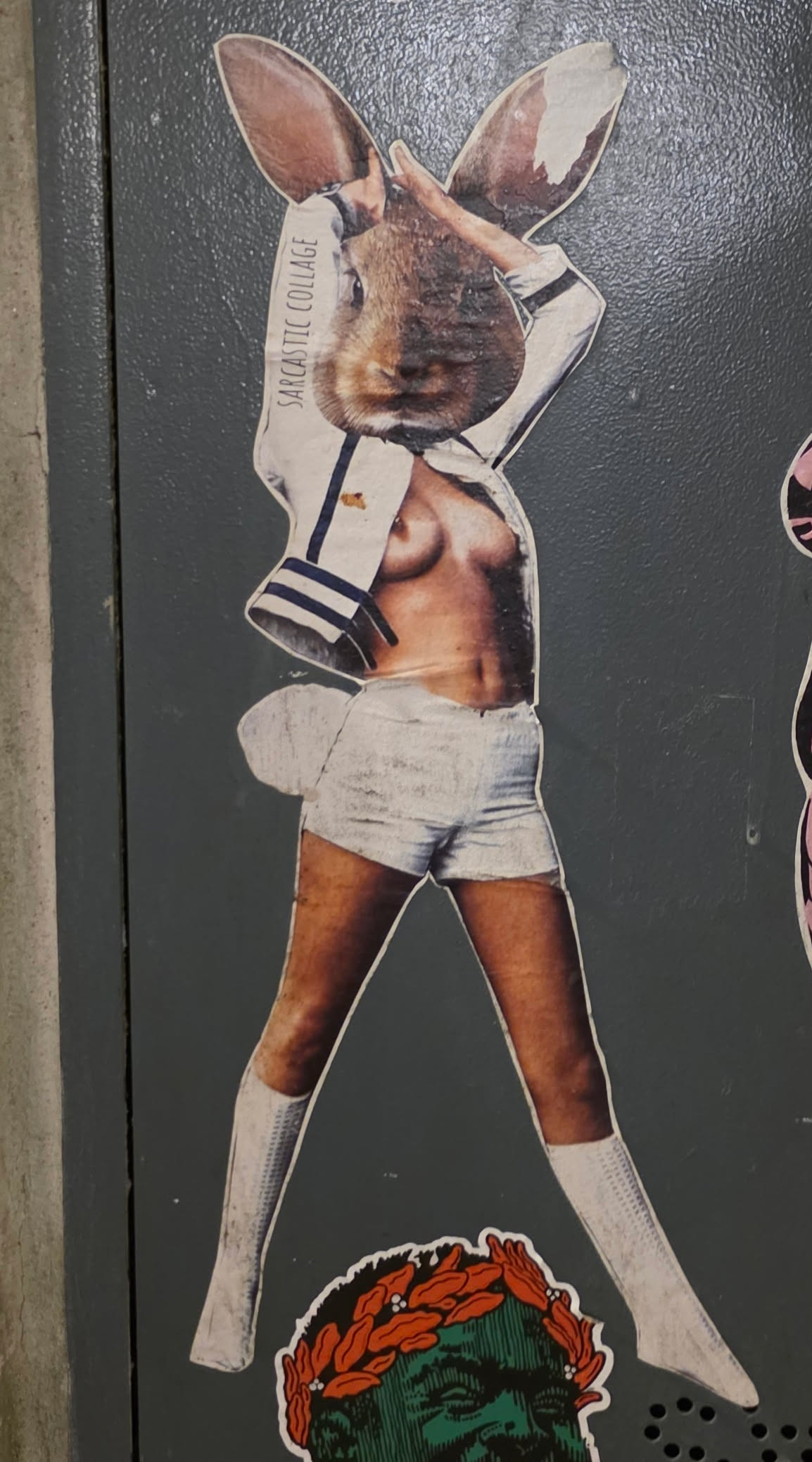 The sticker features a collage of a rabbit's head superimposed onto a human body. The body is depicted wearing a white sailor-style jacket with navy blue trim and white shorts, along with white knee-high socks. The rabbit's ears are prominent, and one hand is raised to its head. The overall aesthetic suggests a vintage or retro feel, with a slightly distressed texture to the printed elements. Below the figure, a portion of another sticker is visible, showing a green-skinned face wearing a laurel wreath.