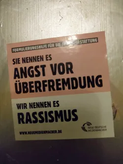 Sticker promoting awareness about racism, stating that what some might call fear of over-foreignization, is actually racism.  The sticker includes the website www.neuemedienmacher.de and the logo of Neue Deutsche Medienmacher (New German Media Makers).