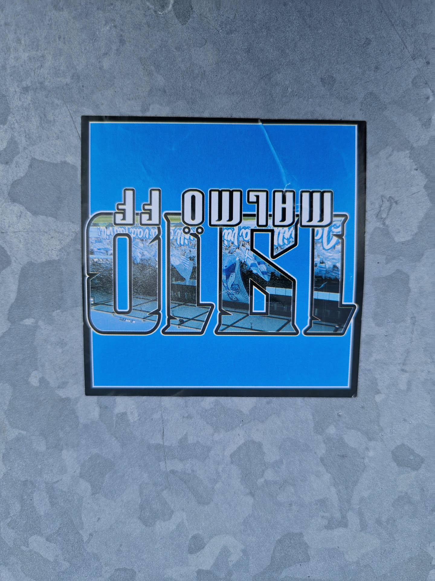 A blue sticker with the word "Olso" in large, stylized letters.  The letters are superimposed on an image that appears to be a postcard or photograph of a snowy scene in Oslo, Norway. The text "MALMO FF" is upside down at the top.