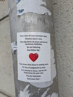 A sticker is posted on a light pole with text in both Swedish and English about Jesus. The text talks about the coming of Jesus and the Day of Judgement.