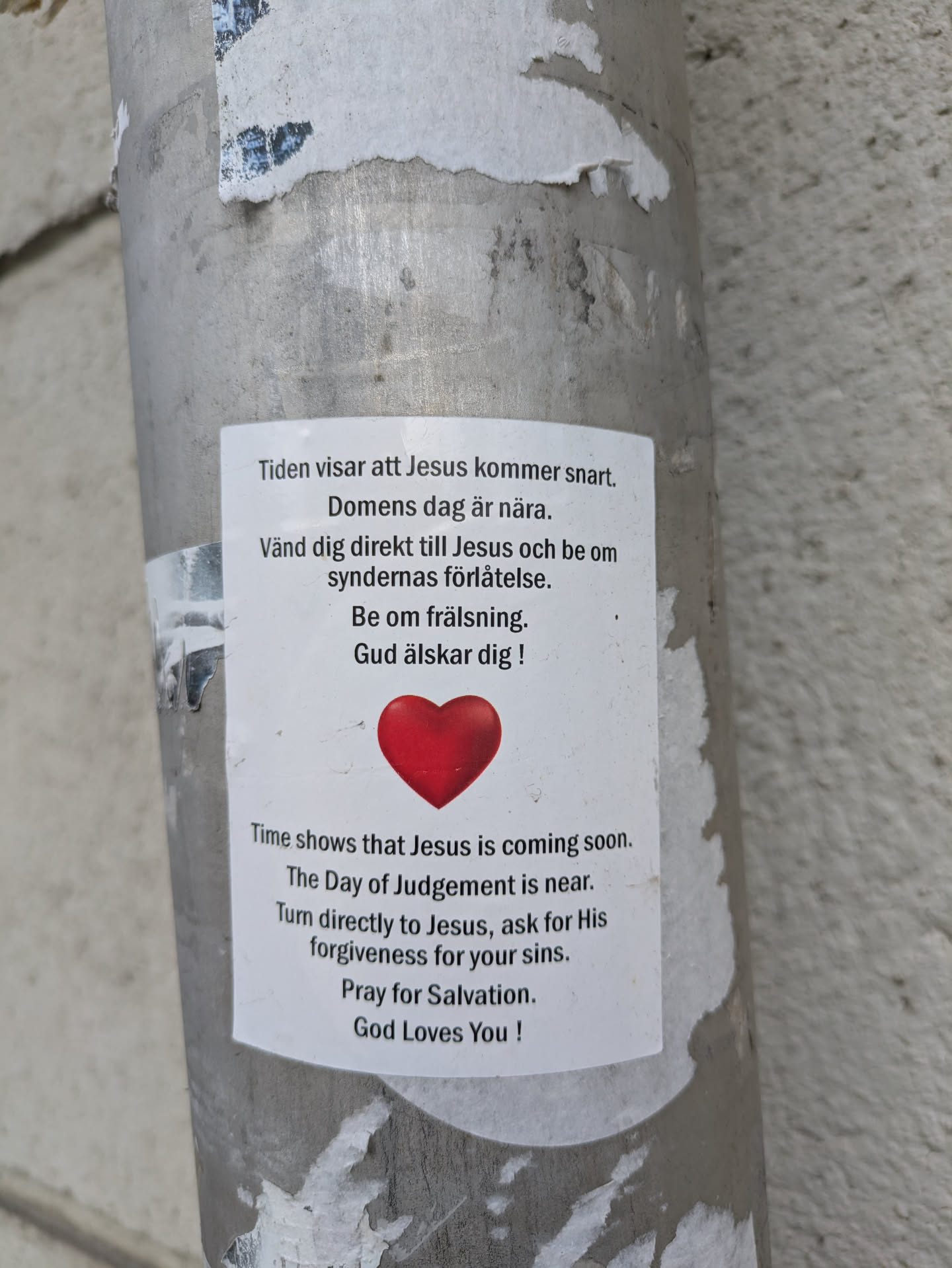 A sticker is posted on a light pole with text in both Swedish and English about Jesus. The text talks about the coming of Jesus and the Day of Judgement.