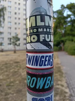 A sticker featuring the text "MLM" with the smaller text "Miro Marlies No Fun" underneath. The sticker has a dark background with light text. It is stuck on a pole with other stickers.