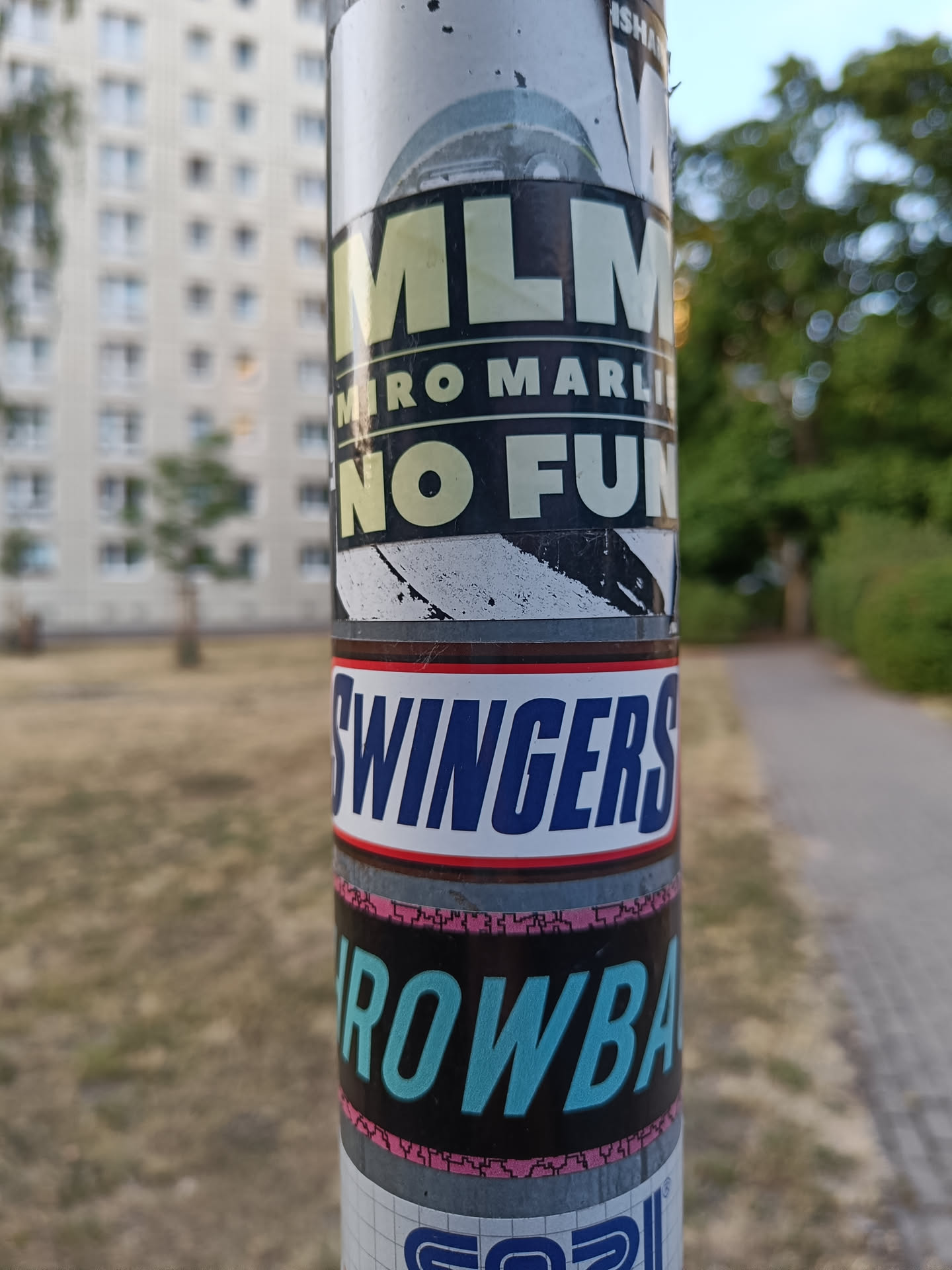 A sticker featuring the text "MLM" with the smaller text "Miro Marlies No Fun" underneath. The sticker has a dark background with light text. It is stuck on a pole with other stickers.