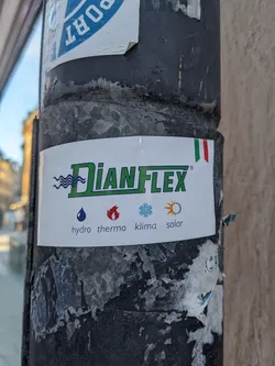 A DianFlex company sticker affixed to a pole. The sticker features the DianFlex logo, and icons representing hydro, thermo, klima, and solar applications. A small Italian flag is also present on the sticker.