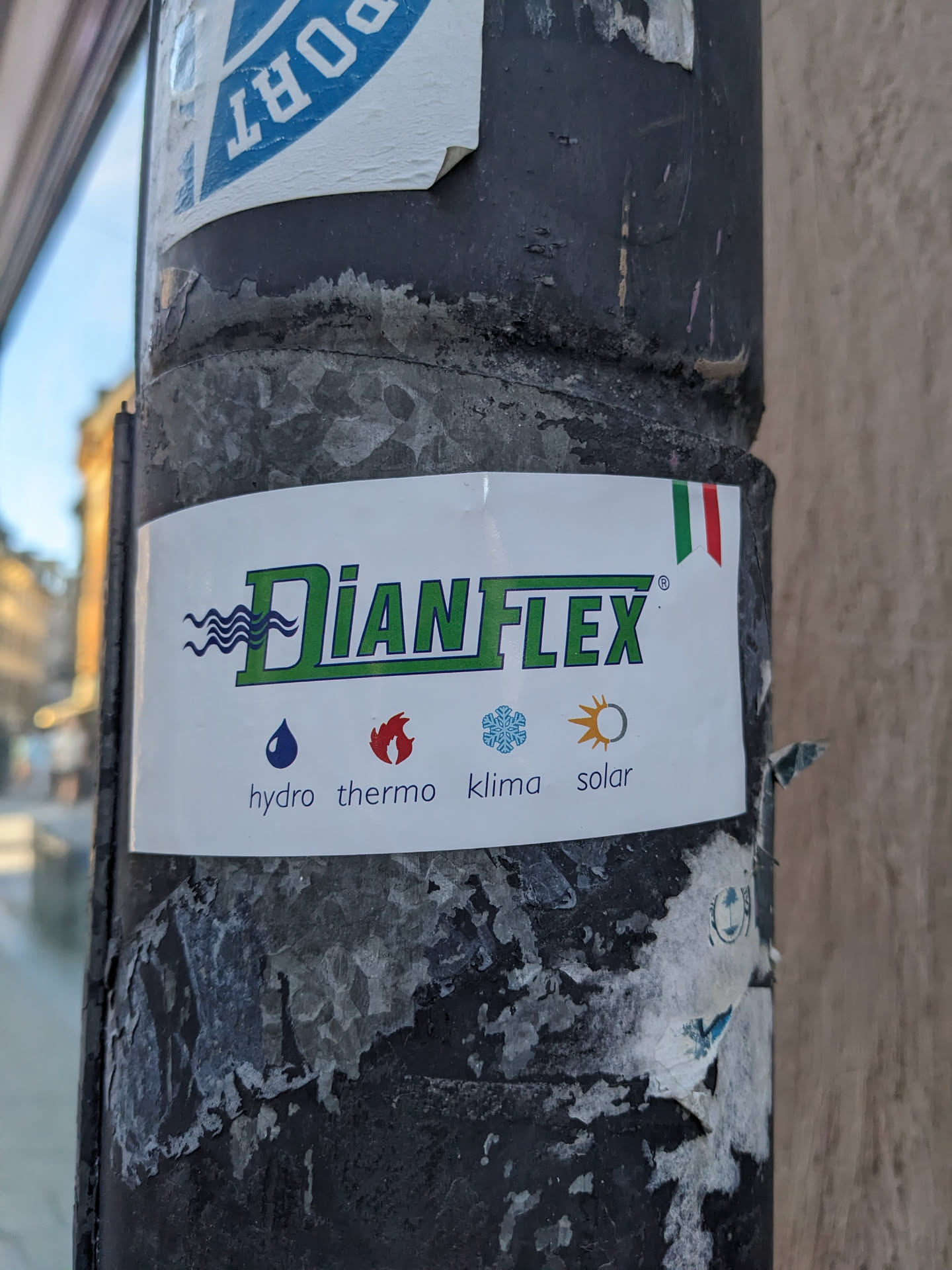 A DianFlex company sticker affixed to a pole. The sticker features the DianFlex logo, and icons representing hydro, thermo, klima, and solar applications. A small Italian flag is also present on the sticker.