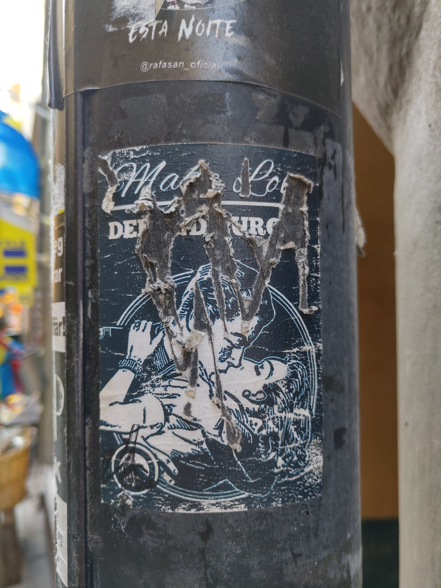 A damaged sticker featuring a black and white illustration of a couple embracing. The text on the sticker is partially obscured due to damage but appears to say "Malo" and other words that are difficult to fully decipher. The sticker shows wear and tear, with parts of the surface peeled off.