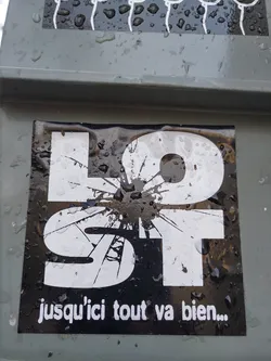 Black and white sticker with the word "LOST" stylized with a cracked effect.  The French phrase "jusqu'ici tout va bien..." (so far, so good...) is written below.