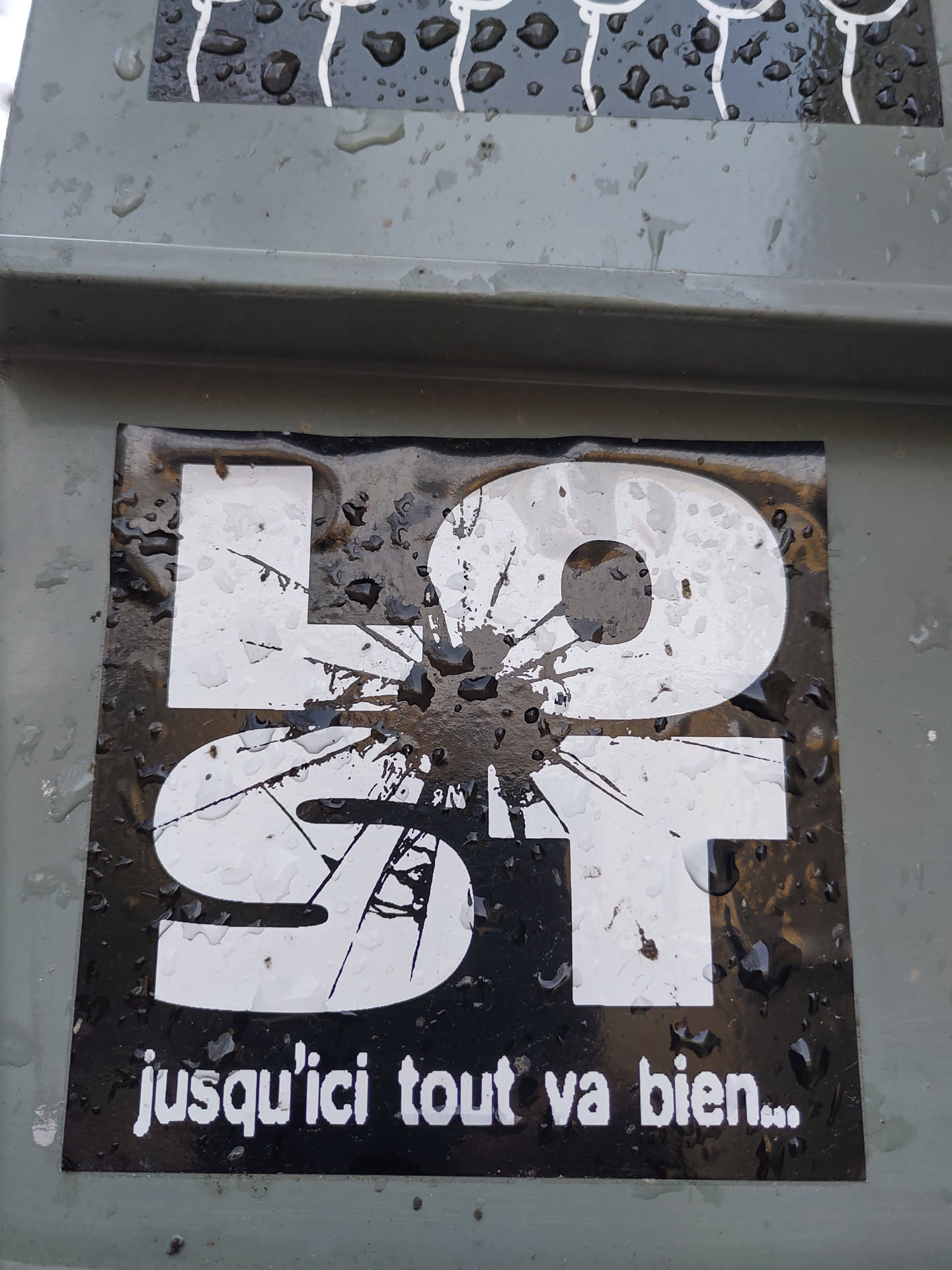 Black and white sticker with the word "LOST" stylized with a cracked effect.  The French phrase "jusqu'ici tout va bien..." (so far, so good...) is written below.