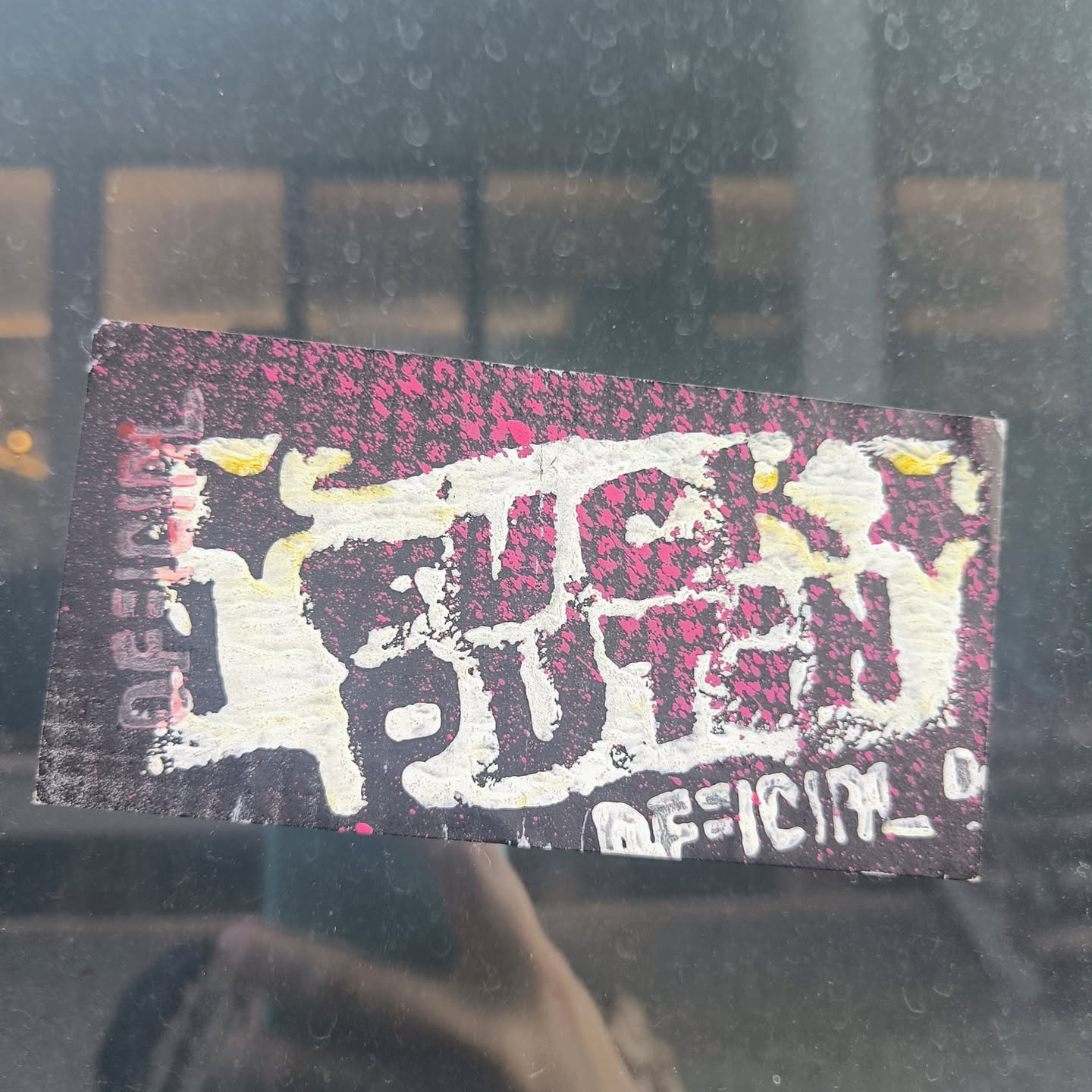 A sticker with the phrase "FUCK PUTIN" in stylized graffiti lettering. The background is dark with pink splatter. The sticker seems to be handmade or DIY style.