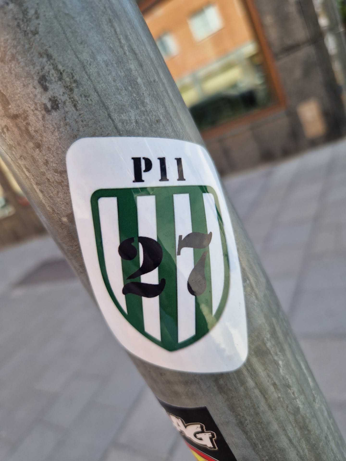 A white sticker with a green and white striped shield design. The number 27 is prominently displayed in black font, with the letters PII at the top.