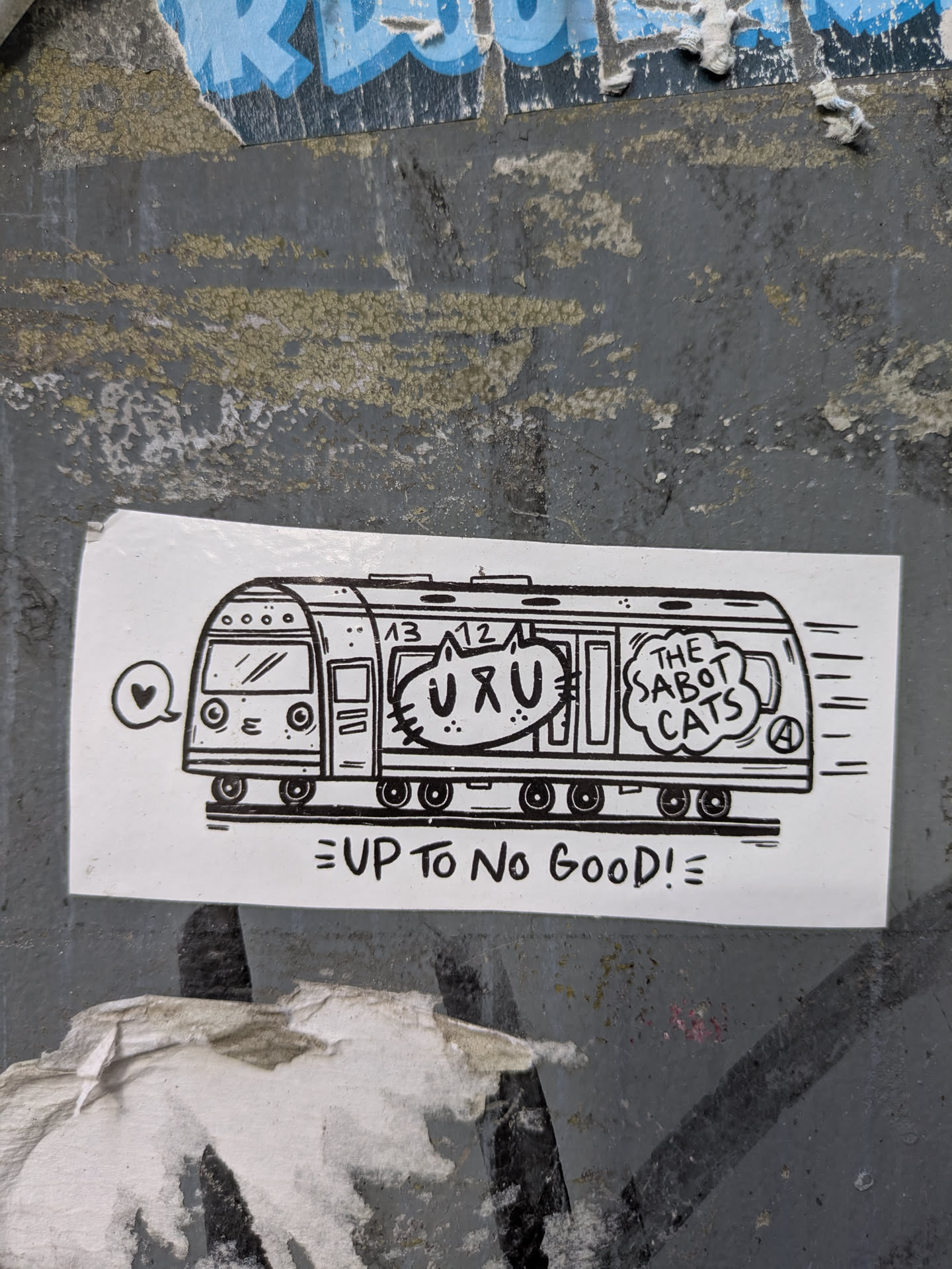 The sticker is white with black line art. It depicts a stylized subway train moving from left to right, indicated by motion lines on the right side. The train's front has a rounded top with four circular windows and a windshield. Inside one of the train cars, a cartoon cat's head is visible, with large eyes and whiskers. This cat appears to be saying "UXU" which is written above its head. Another speech bubble to the right of the cat contains the text "THE SABOT CATS" and what appears to be a stylized "A" in a circle. Below the train, the text "UP TO NO GOOD!" is written in a playful, uneven font, with an exclamation mark and two horizontal lines at the end.