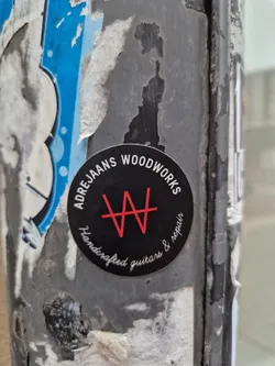A black and red circular sticker with the text "Adre Jans Woodworks" and a logo. It says "Handcrafted guitars & repair" in a smaller font.