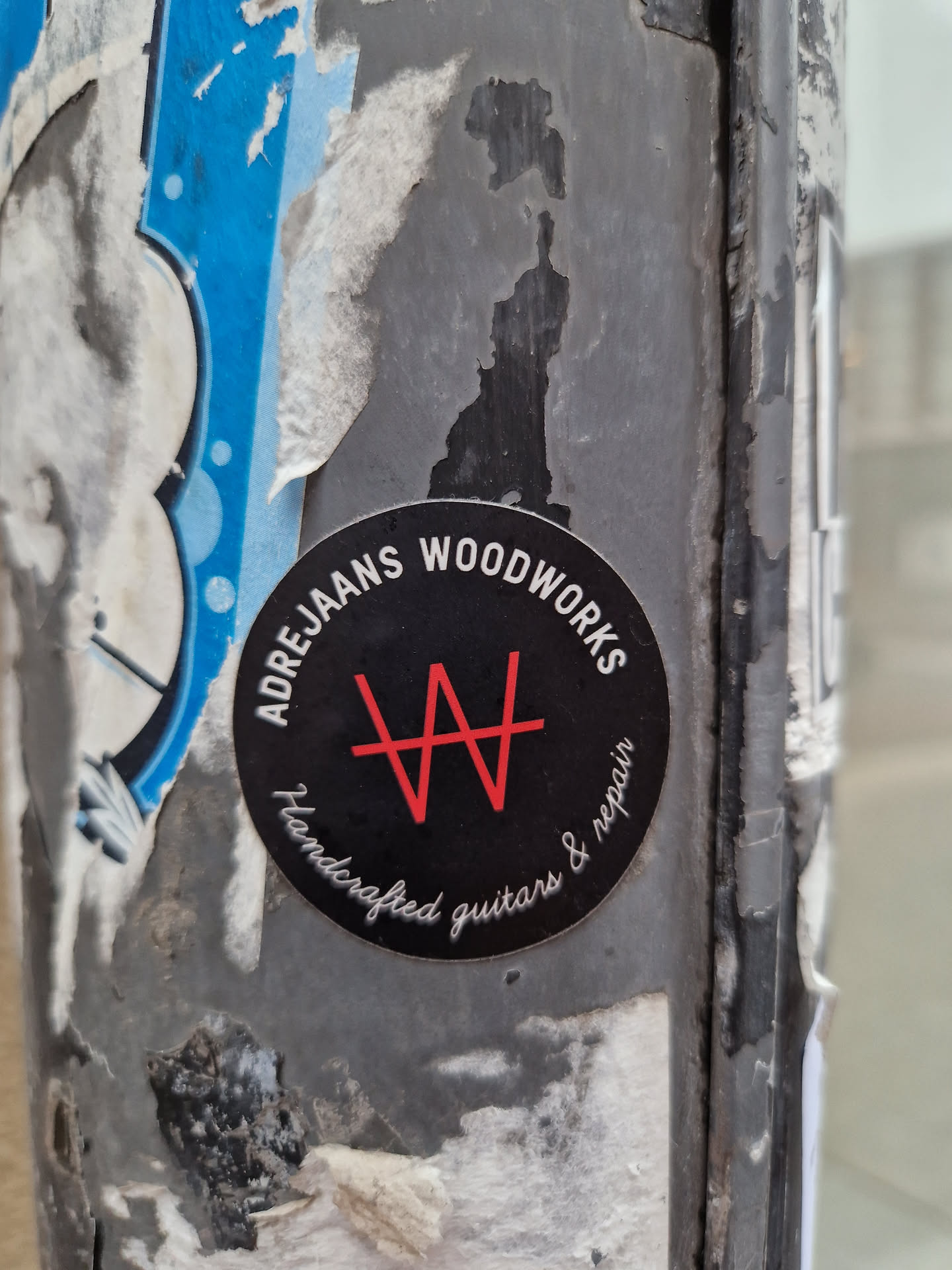 A black and red circular sticker with the text "Adre Jans Woodworks" and a logo. It says "Handcrafted guitars & repair" in a smaller font.