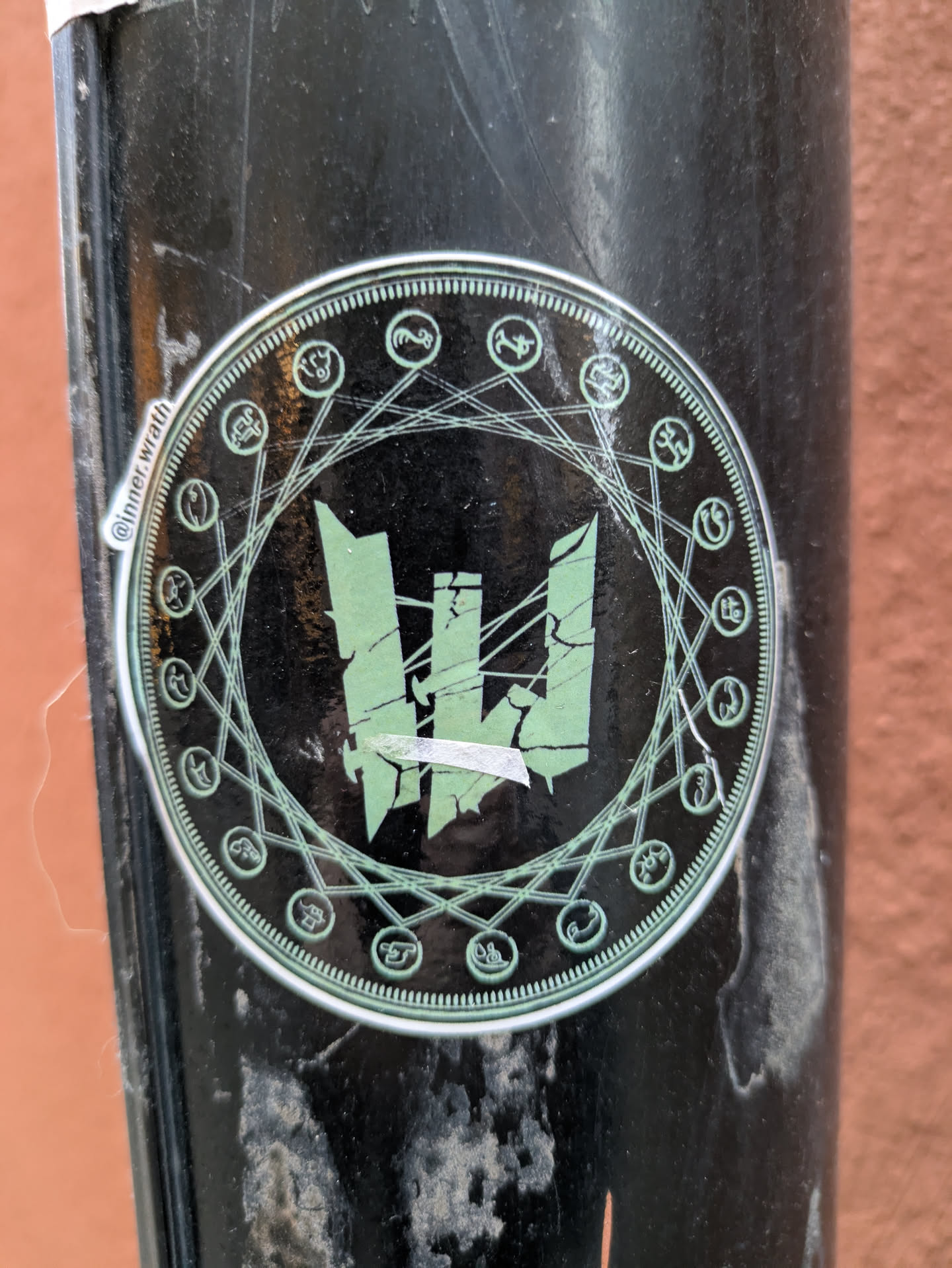 A round sticker with a dark background and a central design of a stylized, fractured letter "W." The "W" is surrounded by a circular frame with various symbols and connecting lines, suggestive of occult or esoteric symbolism. The text '@Inner Wrath' is visible on the left side of the sticker.