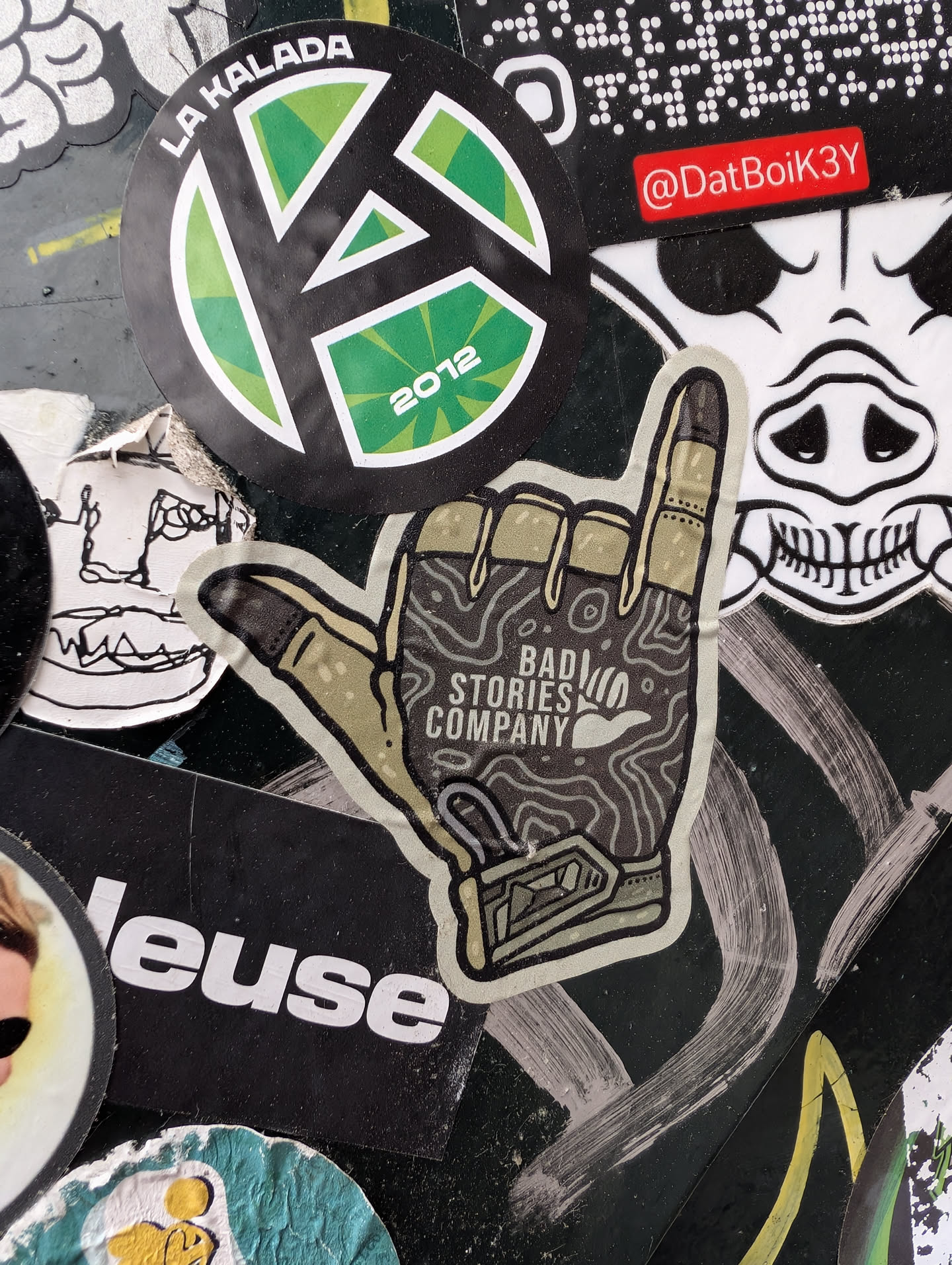 This sticker for 'Bad Stories Company' shows a hand gesture, specifically the 'rock on' or 'devil horns' sign, rendered in a topographic map style with earthy tones. The company's name is printed within the hand's palm area.