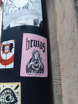 Street sticker Pink sticker with black and white illustration of Virgin Mary holding a heart. The word "brujas" is written in a gothic style font at the top. There is a website address at the bottom.