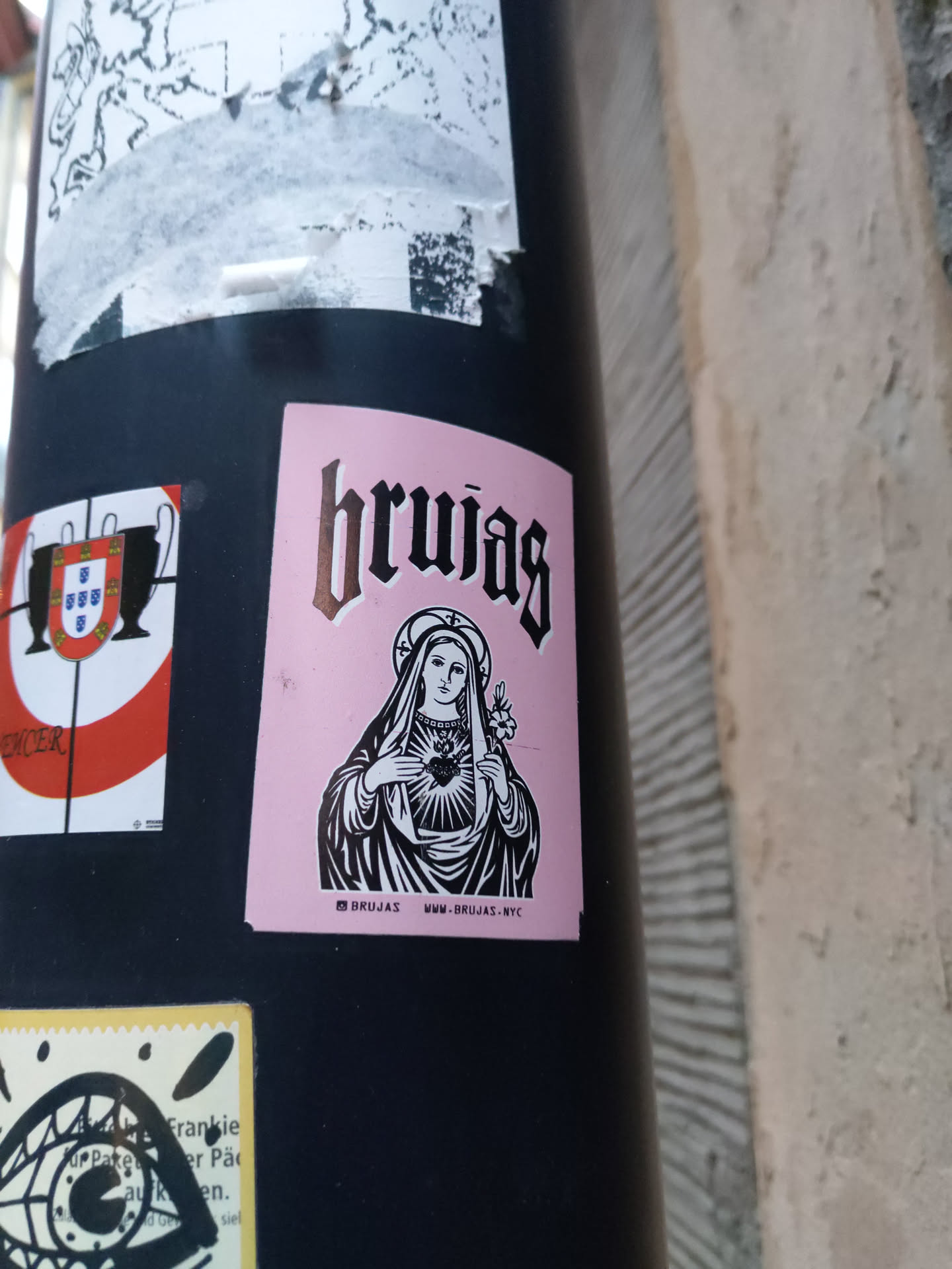 Pink sticker with black and white illustration of Virgin Mary holding a heart. The word "brujas" is written in a gothic style font at the top. There is a website address at the bottom.