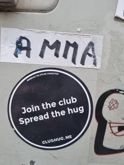 Round black and white sticker with the text "Join the club Spread the hug" and the website address ClubHug.me.  The text "Embrace the offline connection" is also visible in smaller font above the main text.