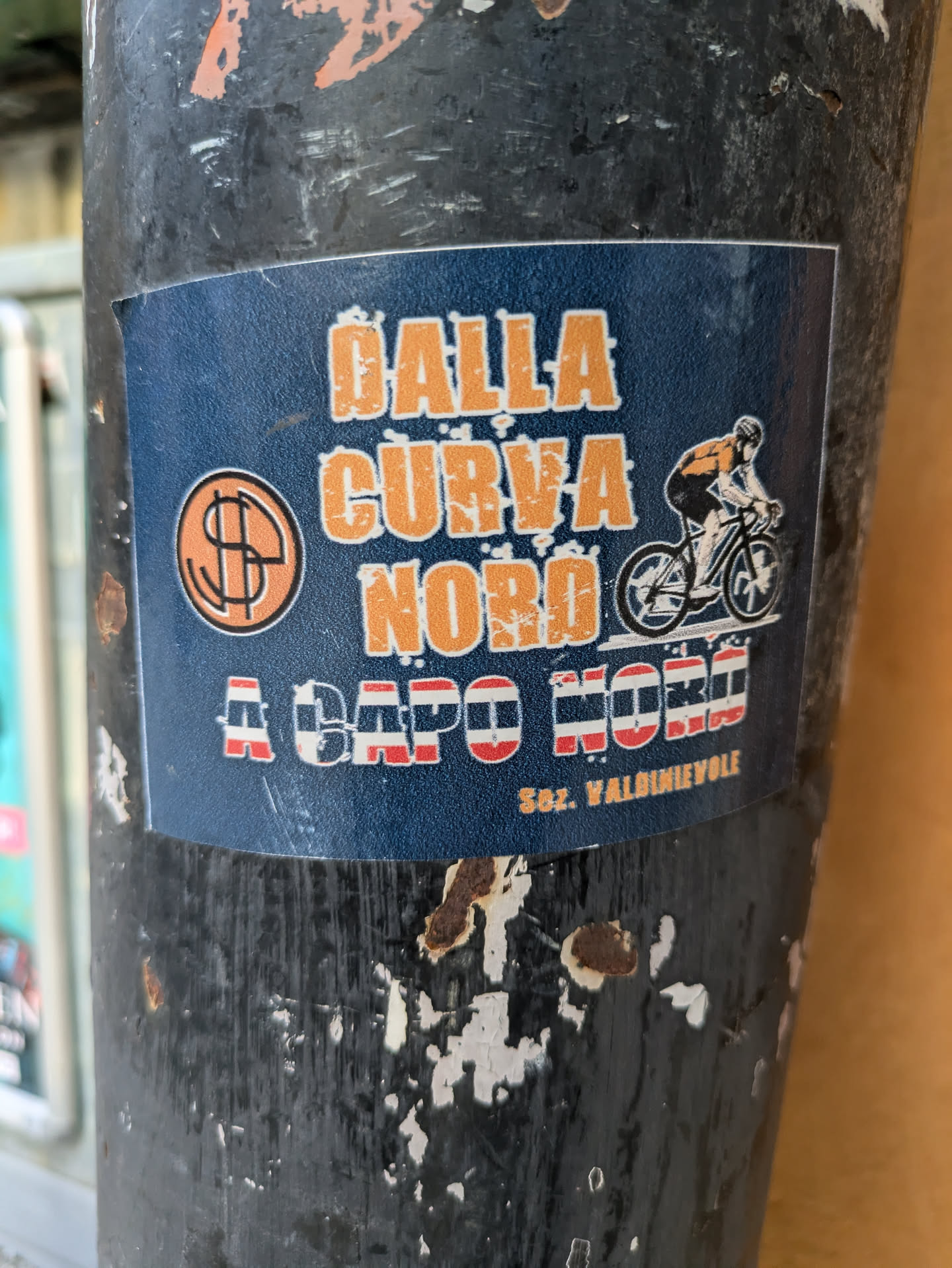 A sticker featuring a cyclist riding a bicycle, with text in Italian that translates to "From the North Curve to Capo Nord." It also features a stylized dollar sign.