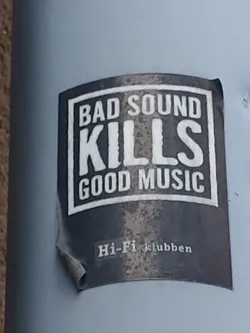 A sticker with a strong message about sound quality.  The sticker is dark gray or black with white text. It's slightly worn and peeling at the edges.
