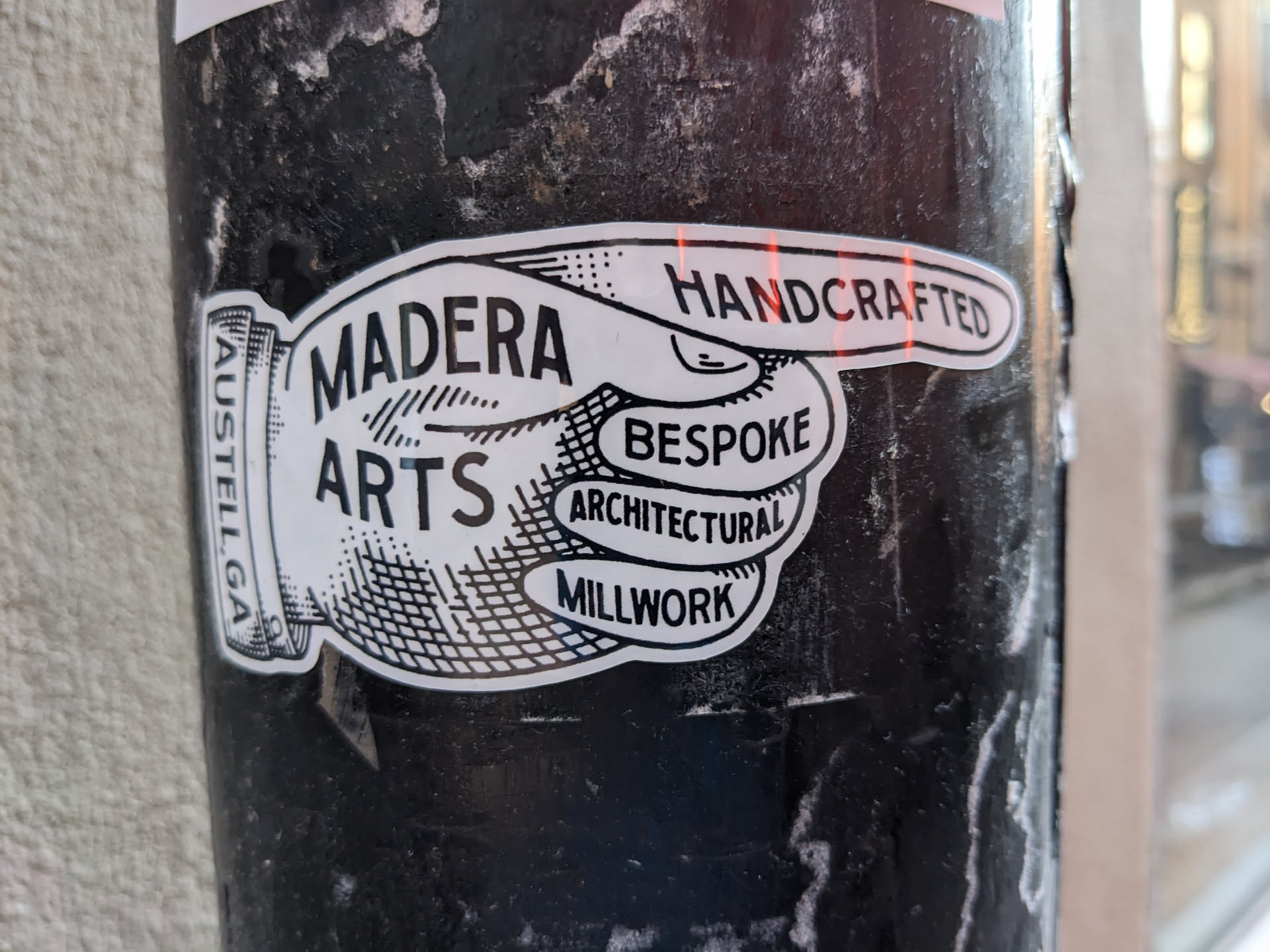 A black and white sticker featuring a hand pointing to the right with the words Madera Arts.  Other words on the sticker include Handcrafted, Bespoke, Architectural and Millwork. There is also smaller text that says Austell, Ga.