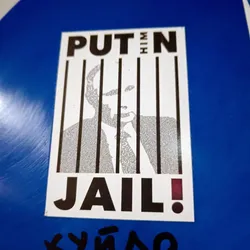 A sticker depicting Vladimir Putin behind bars. The image of Putin is composed of small text.  The sticker has a strong anti-Putin message.